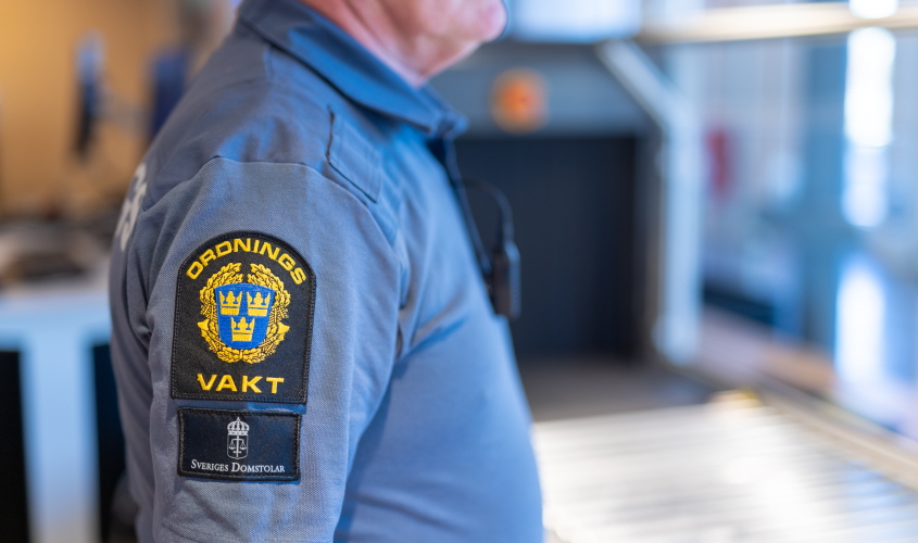 Närbild på en ordningsvakts uniform, emblem och telefon syns