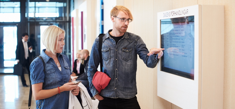 Två personer står vid en skärm som visar dagens förhandlingar i domstolen.  Foto.